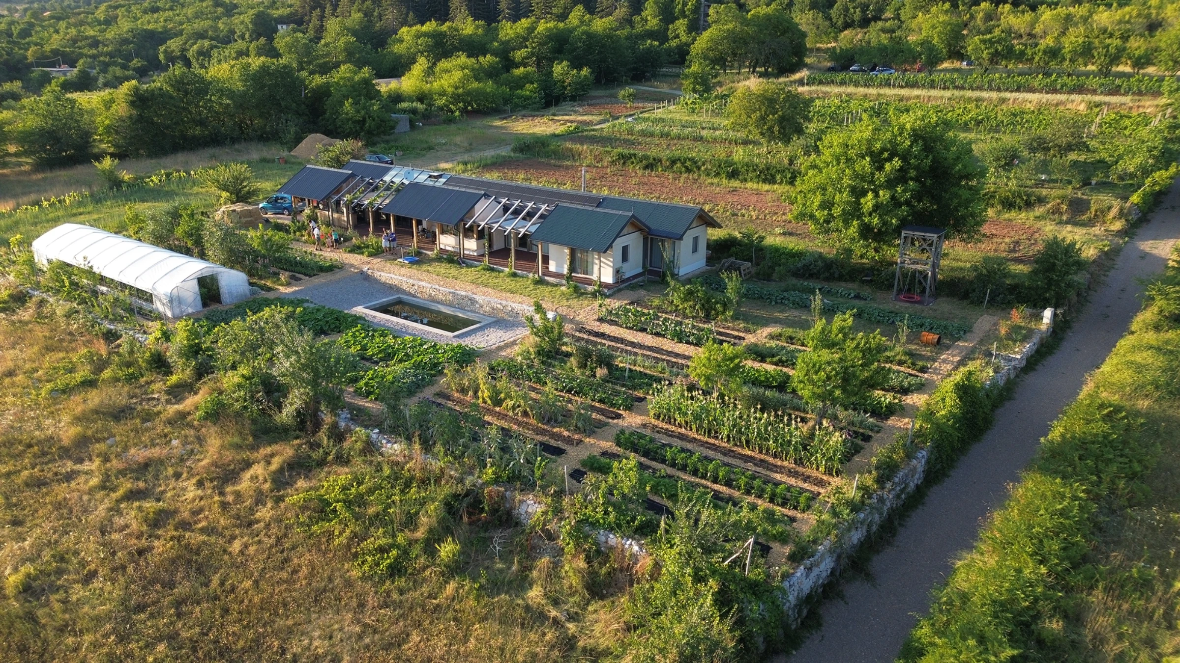 Aerial view of Mikrofarma Mrvica at golden hour: house, greenhouse, and biointensive garden rows